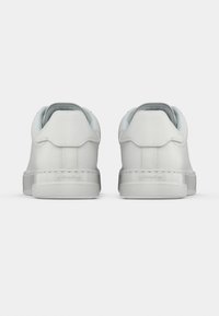 Λευκά δερμάτινα αθλητικά παπούτσια με λείο υλικό, στρογγυλεμένο σχήμα, ανοιχτό μπλε λεπτομέρειες στο εσωτερικό και λογότυπο στην πτέρνα. Μινιμαλιστικός σχεδιασμός.