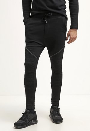 Zwarte joggingsbroeken met een tapered fit. Voorzien van gewatteerde accenten, ritszakken en een trekkoord in de taille. Te combineren met zwarte sneakers.