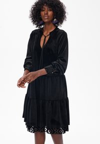 Czarna sukienka z weluru o warstwowym kroju, z długimi rękawami i akcentami w leopardzi wzór na mankietach. Posiada zapięcie na kokardę przy dekolcie.