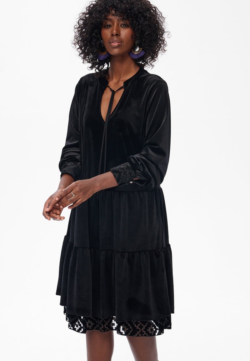 Czarna sukienka z weluru o warstwowym kroju, z długimi rękawami i akcentami w leopardzi wzór na mankietach. Posiada zapięcie na kokardę przy dekolcie.