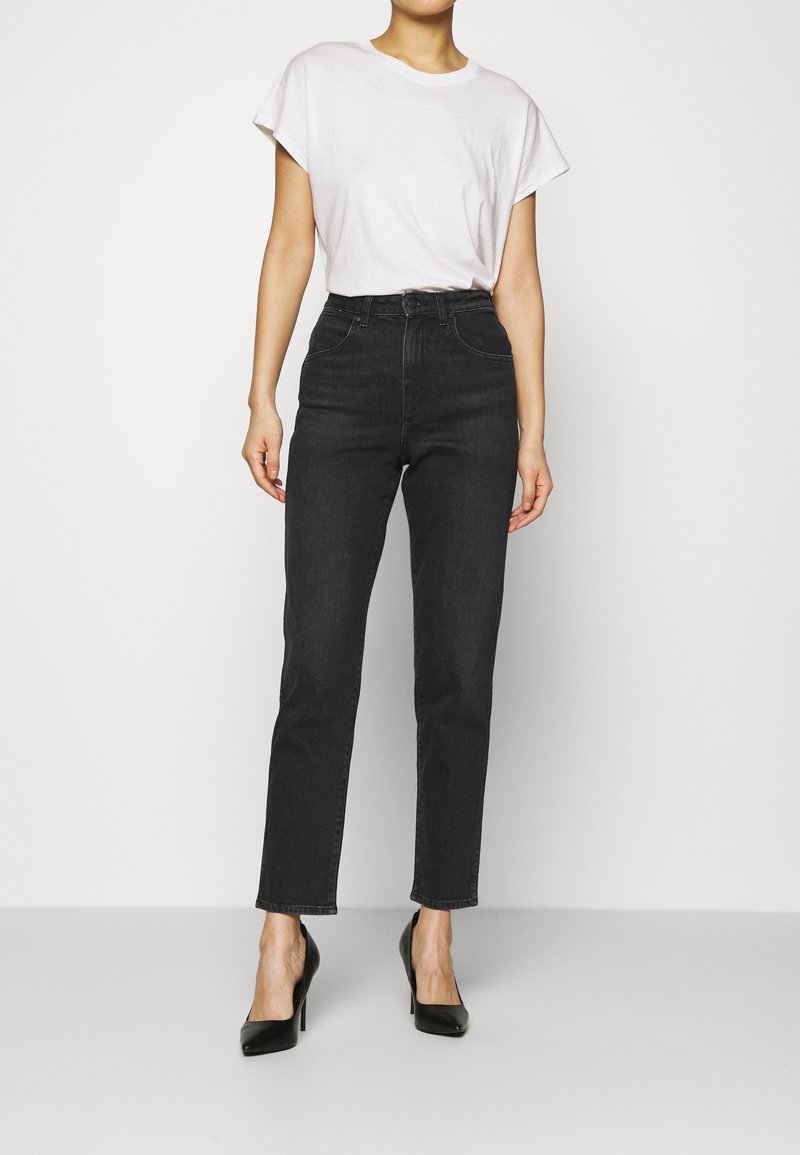 Högmidjade svarta jeans med smal passform, med dragkedja och fem fickor, tillsammans med en vit t-shirt med kort ärm och svarta klackar.