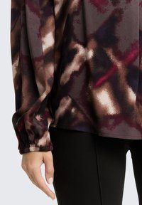 Long-sleeved top in a textured fabric with a dark multicolored abstract pattern; gathered cuffs and a relaxed fit, paired with black leggings.