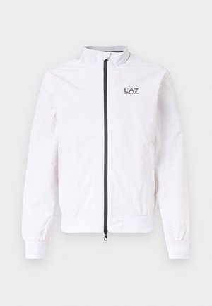 Fehér cipzáras dzseki magas gallérral, rugalmas mandzsettákkal és alsó szegéllyel, valamint fekete EA7 Emporio Armani logóval a bal mellrészen.