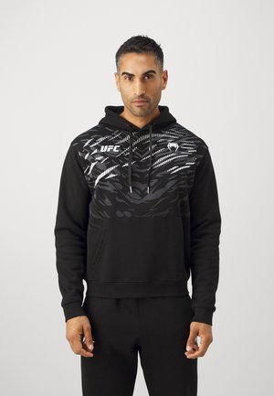 Black hoodie features a textured, patterned upper with white accents and a kangaroo pocket. Drawstrings and UFC logo on chest.