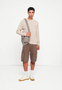 Beżowy sweter o fakturze, brązowe szorty cargo z bocznymi kieszeniami, białe i brązowe sneakersy, szara torba na ramię. Minimalistyczne tło.