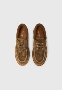 Καφέ σουέντ παπούτσια με κορδόνια, με φούντες στο εμπρός μέρος και ορατές λευκές ραφές, σε λευκό φόντο, φωτογραφημένα από πάνω.