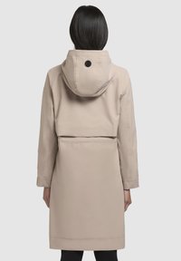 Beige buitenkleding met een capuchon, voorzien van een getailleerde taille en een gladde textuur. Inclusief een zwarte knoopaccent aan de achterkant.
