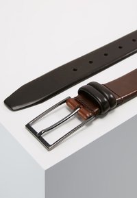 Set de ceintures en cuir avec une sangle noire et une sangle marron, ornées d'une boucle en métal argenté et d'une touche en cuir. Texture lisse, design minimaliste.