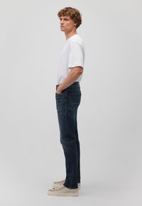 Schmal geschnittene dunkelblaue Denim-Jeans mit klassischem Fünf-Taschen-Design, kombiniert mit einem weißen T-Shirt mit kurzen Ärmeln und beigen Sneakern.