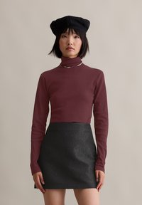 Bordeaux langemouw turtleneck shirt gecombineerd met een zwarte textuur mini-jurk en een zwarte baret, geaccentueerd met een zilveren ketting.