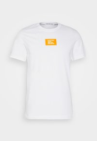 Bílý bavlněný tričko s čtvercovým oranžovým logem na levé straně hrudi. Kulatý výstřih, krátké rukávy a hladká textura.