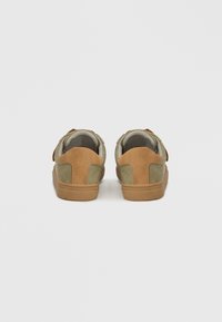 Zielono-brązowe tenisówki z cholewką wykonaną ze zamszu i tkaniny, wyposażone w wyściełany kołnierz i beżową gumową podeszwę, widziane od tyłu.