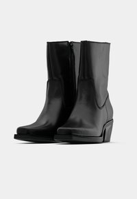 Melni ādas potīšu zābaki ar gludu apdari, kvadrātveida purngaliem un zemu platformas papēdi. Satur sānu rāvējslēdzēju un minimālisma dizainu.