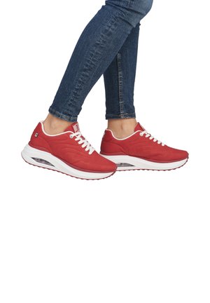 Red athletic shoes with a mesh upper, white laces, and cushioned sole featuring a visible air unit. Worn with dark blue fitted jeans.