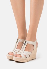 Sandalias de cuña beige con suela de yute trenzado, que cuentan con un cierre de cremallera y múltiples tiras de tela sobre el pie para brindar soporte y estilo.