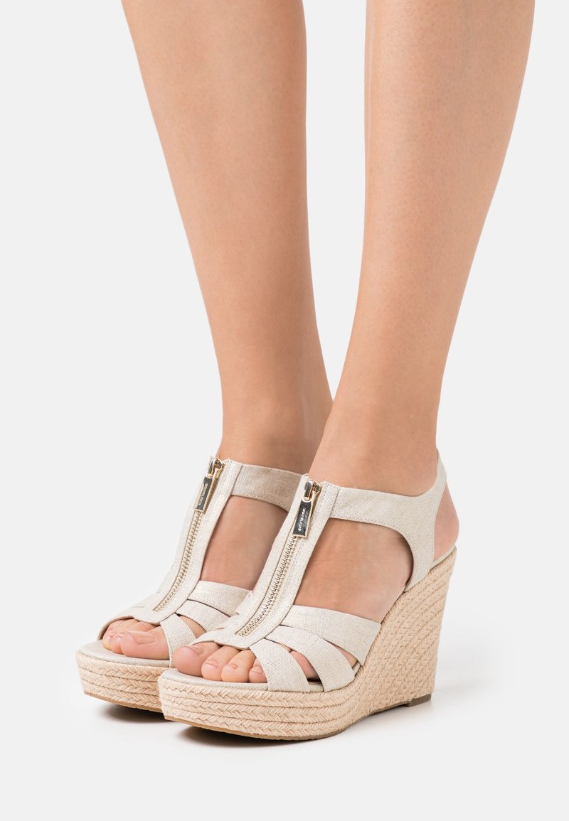 Sandalias de cuña beige con suela de yute trenzado, que cuentan con un cierre de cremallera y múltiples tiras de tela sobre el pie para brindar soporte y estilo.