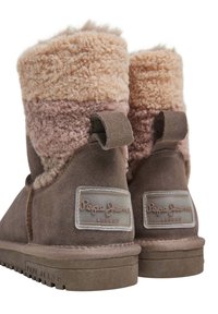 Botas de tobillo de ante marrón con un puño de borrego esponjoso en beige y rosa, que cuenta con un parche de logotipo y una lengüeta en la parte posterior. Suela de goma plana.