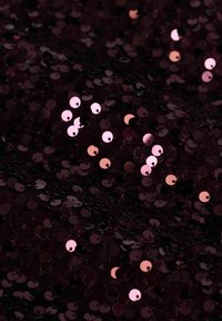 Bordeauxfarbener Stoff bedeckt mit runden, glänzenden Pailletten in verschiedenen Schattierungen von Rosa und Schwarz, die eine strukturierte, reflektierende Oberfläche schaffen.