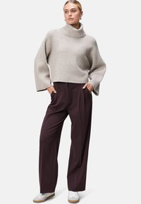 Helle graue gerippte Strickjacke mit hohem Kragen und weiten Ärmel, kombiniert mit dunkelburgunderfarbenen Palazzo-Hosen und weißen Sneakers.