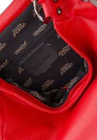 Red leather handbag interior with a zipper pocket. Black lining features repeating "VENEZIA" logo. Textured exterior and smooth hardware.