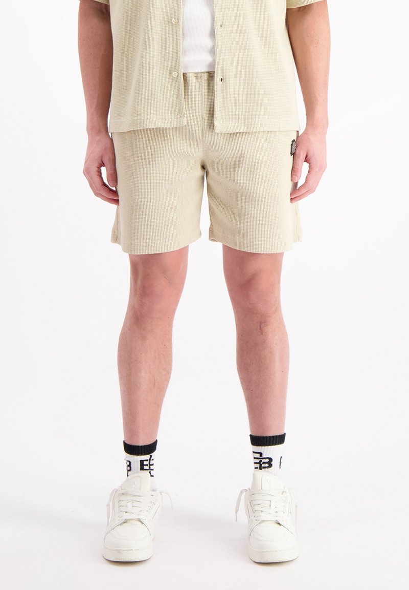 Lichtbeige shorts van een gestructureerde stof, met een elastische tailleband en zijzakken, gecombineerd met een bijpassend T-shirt met korte mouwen.