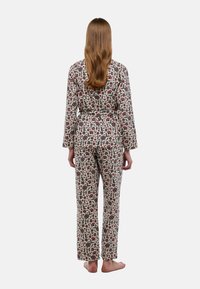Ensemble de pyjama à imprimé floral comprenant des manches longues et un pantalon, fabriqué dans un tissu léger. Les couleurs incluent crème, rouge et vert. Inclut une ceinture à nouer.