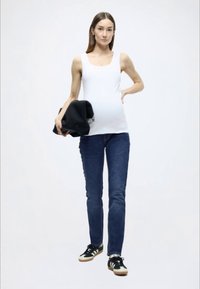 Λευκό αμάνικο μπλουζάκι, στενά τζιν σε σκούρο μπλε χρώμα, μαύρο σακάκι στο χέρι και μαύρα αθλητικά παπούτσια με λευκές και καφέ λεπτομέρειες. Απλές, καθαρές γραμμές.