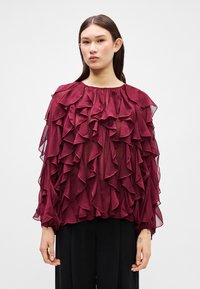 Maroon ruffle blouse with sheer fabric, high neckline, and long sleeves. Features layered ruffles across the front and upper sleeves.