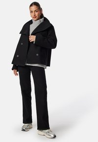 Svart ullblandad dubbelknäppt kappa med överdimensionerad krage, kombinerad med en grå turtleneck och svarta byxor, prydd med silverfärgade sneakers.