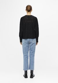 Pull noir texturé avec un motif en dentelle, manches ballon et col arrondi, associé à un jean droit bleu clair et des bottes noires.