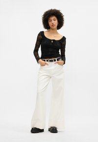 Μαύρο εφαρμοστό μπλουζάκι με μακριά μανίκια, φλοράλ υφή και λεπτομέρεια με κορδόνι, σε συνδυασμό με λευκά παντελόνια σε φαρδιά γραμμή και χοντρά μαύρα παπούτσια με πλατφόρμα.