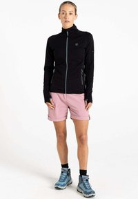 Schwarze Zip-Jacke mit hohem Kragen und hellblauen Akzenten; kombiniert mit pinken Shorts und grauen Wanderschuhen. Glatter Stoff, taillierte Passform.