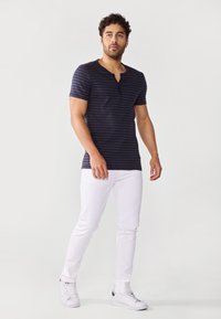 Camisa de rayas azul marino de manga corta con cuello abotonado, combinada con jeans blancos de corte ajustado y zapatillas blancas.