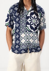 Camicia a maniche corte blu navy con motivi geometrici in bianco e verde, dotata di una chiusura frontale con bottoni e un fit rilassato.