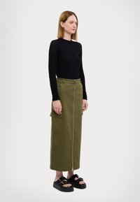 Top lungo a maniche lunghe nero a coste abbinato a una gonna lunga verde oliva con zip frontale e tasche cargo. Sandali platform neri.