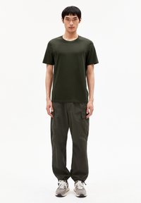 Olive green crew-neck t-shirt with short sleeves, paired with loose-fitting olive cargo pants featuring side pockets. Gray and white sneakers.