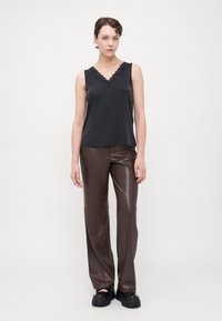 Top negru fără mâneci cu decolteu în V cu margini ondulate și pantaloni din piele sintetică maro. Țesătură texturată cu o finisare netedă, completată cu pantofi grozavi negri.