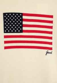 Pletený svetr s motivem vlajky USA v červené a námořnické modři na krémovém pozadí, s výšivkou "Gant" v námořnické modři.