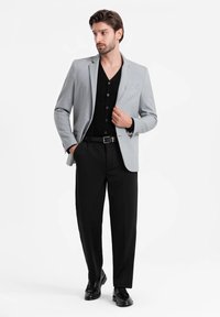 Męska jasnoszara marynarka na czarną koszulę zapinaną na guziki, zestawiona z czarnymi spodniami i czarnymi butami. Slim fit, gładki materiał i zorganizowany krój.