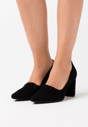 Schwarze Wildleder-Pumps mit spitzem Zehenbereich und abgerundeter Front, ausgestattet mit einem stabilen Blockabsatz. Glatte Textur.