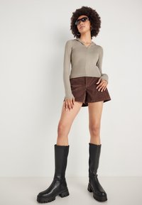 Lys oliven langærmet hoodie, brune ruskindsshorts og knæhøje sorte læderstøvler med en kraftig sål. Solbriller og hoops inkluderes.
