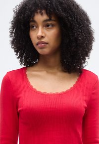 Haut rouge à manches longues avec une texture côtelée, un col festonné et un motif à petits points subtil, adapté à une tenue décontractée.