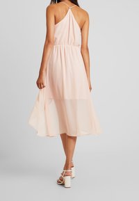 Ljusrosa, midilång klänning med halterneck, draperad midja och genomskinligt tyg. Matchas med vita klacksandaler med blockklack.