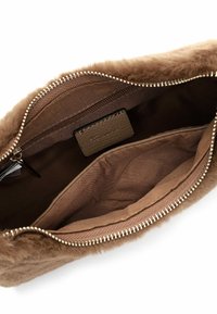 Ruskea tekoturkis clutch-laukku, jossa on vetoketjullinen yläosa, sileä sisävuori ja pieni taskulappu. Pintarakenteinen ulkopinta ja metallivetoketju.