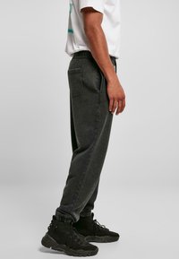 Mørkegrå joggebukser med elastisk talje, sidelommer og ribbede cuffs, parret med sorte sneakers. Mat tekstur.