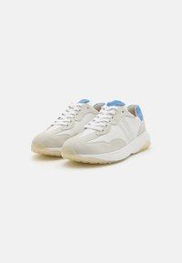 Lys grå sneakers med overdel i semsket skinn og lær, blå detaljer på hælen, hvite lisser og en beige gummisåle.