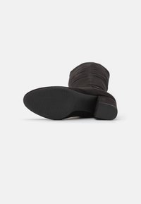 Bottine en daim noir avec un bout rond, une semelle texturée et un petit talon. Le design présente de douces fronces le long de la tige.