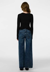 Melns tops ar garām piedurknēm un pieguļošu vidukļa daļu, savienots ar platām, augsta vidukļa zilā džinsa biksēm ar aizmugurējām kabatām un izbalējušu tekstūru.