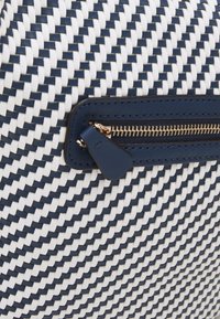 Sac tissé présentant un motif bleu marine et blanc, avec une finition texturée et un accent de fermeture éclair dorée sur un contour en cuir bleu marine.