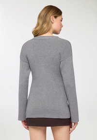 Maglione grigio a coste con maniche lunghe, scollo ampio e orlo posteriore leggermente allungato. Tessuto morbido e design aderente.